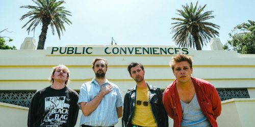 A Swayze & The Ghost - 4 punk dudes in front of an old art deco building with a clear sky and palms in the background