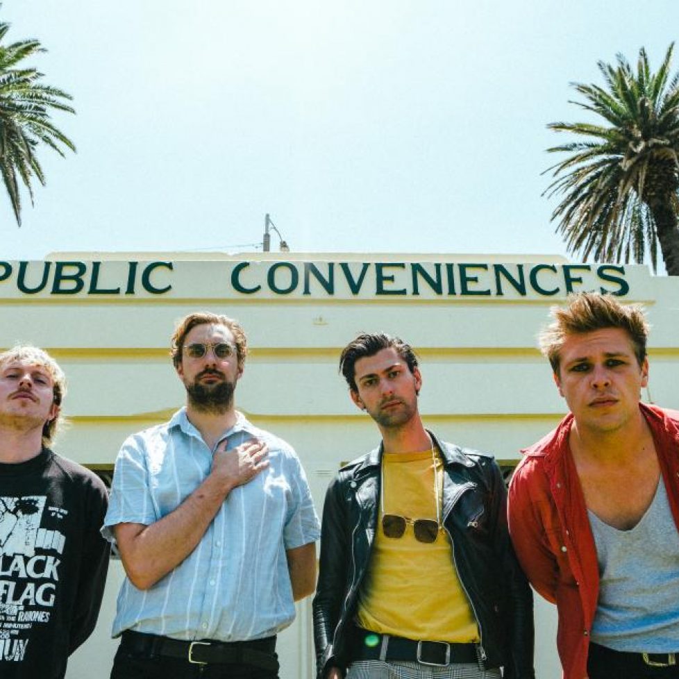 A Swayze & The Ghost - 4 punk dudes in front of an old art deco building with a clear sky and palms in the background