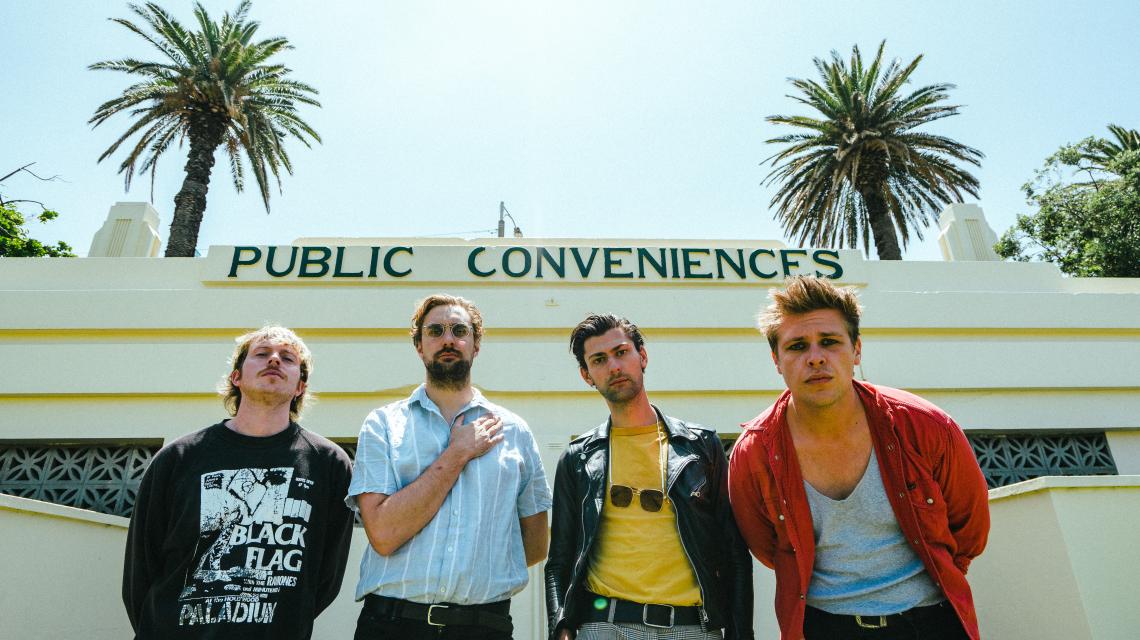 A Swayze & The Ghost - 4 punk dudes in front of an old art deco building with a clear sky and palms in the background